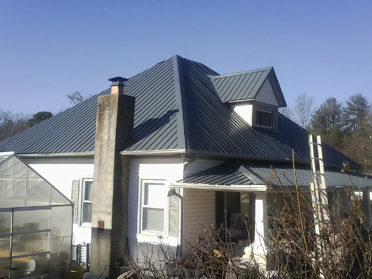 Dark blue standing seam metal roof on a white farmhouse with dormer — Slate & Tile Roof Repair by Roofing Brothers in Kiln
