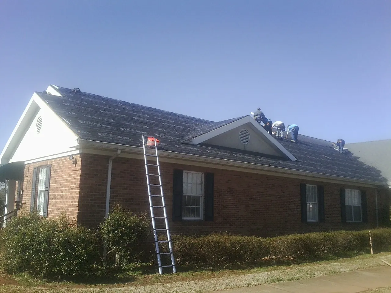 Crew tearing shingles off a brick ranch roof with a ladder set — Metal Roof Repair work by our crew in Kiln