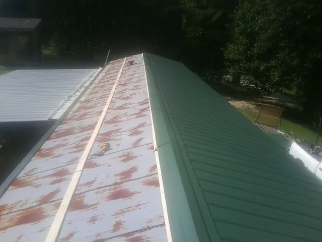 Old rusted panels beside newly installed green metal roofing — Wind Damage Roof Repair by Roofing Brothers in Kiln