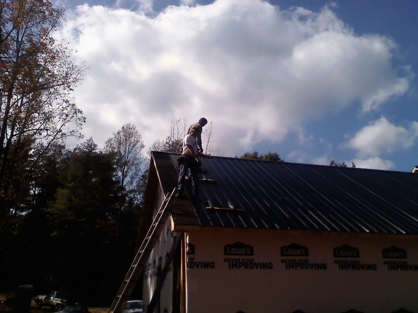 Roofer fastening dark metal panels high against a cloudy sky, from a Roof Inspection job in Kiln