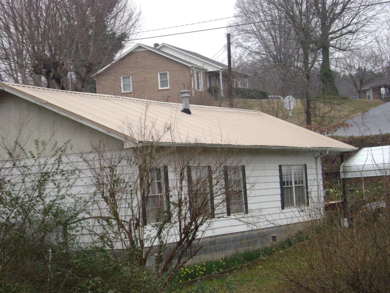 Tan metal roof on a white sided house set into a hillside — Commercial Roofing by Roofing Brothers in Kiln