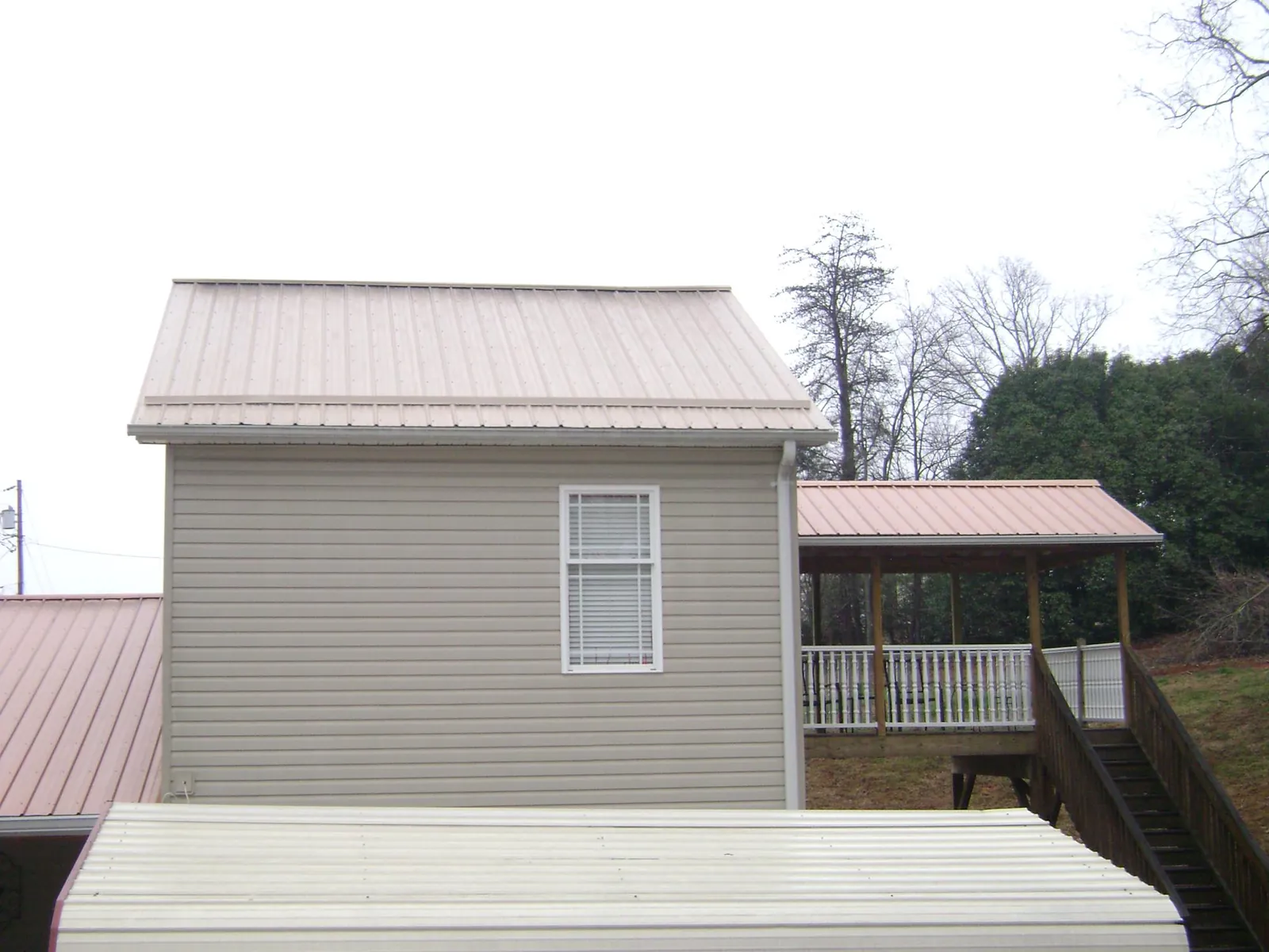Tan metal roofs on a two story addition and attached porch, from a Roof Replacement job in Kiln